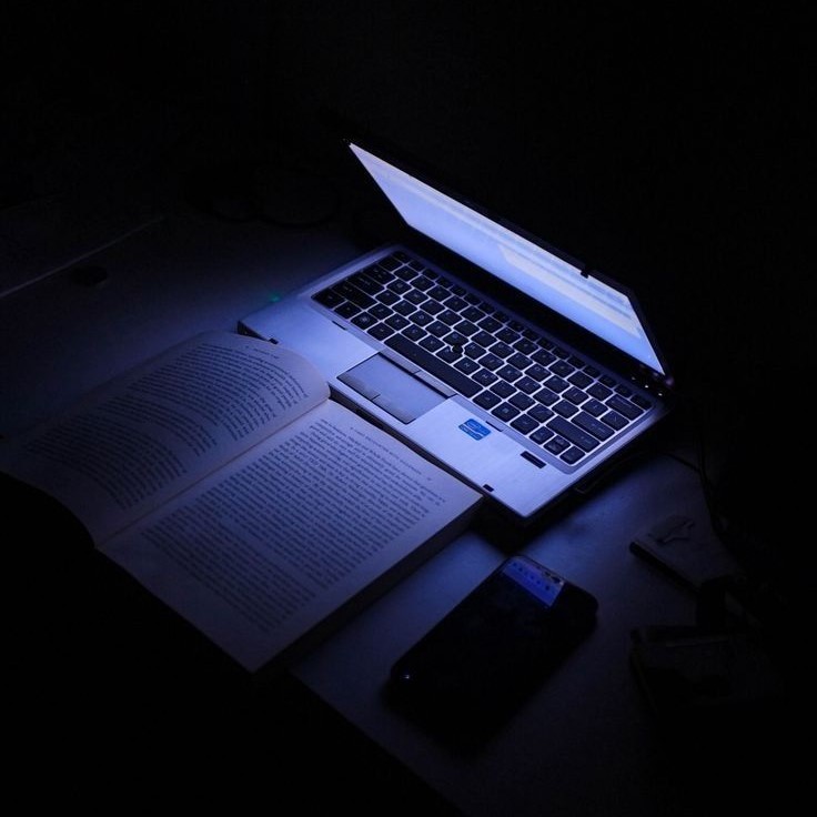 Ноутбук в темноте, освещеющий книгу